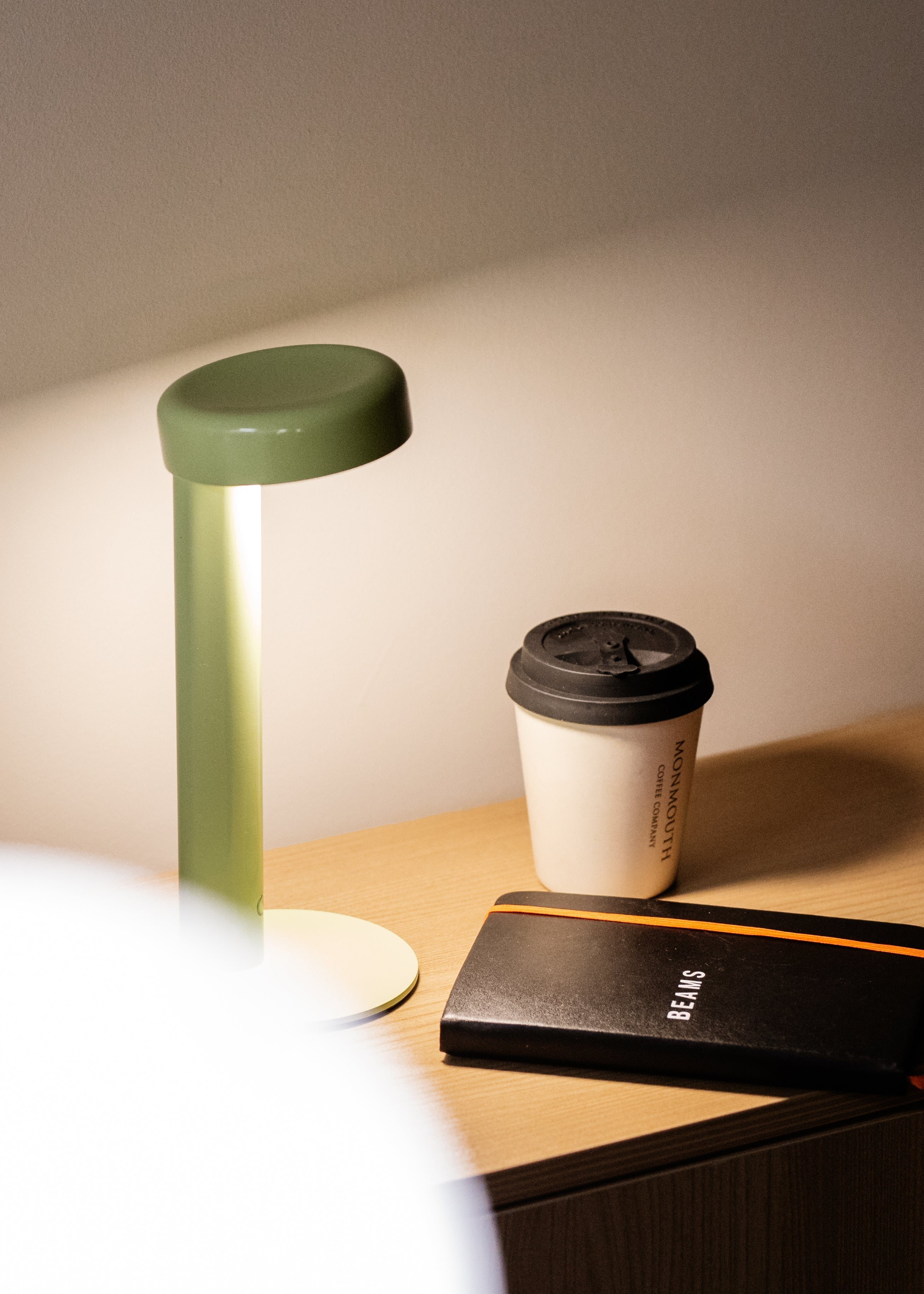 Small green lamp on a wooden surface with a cup and phone in the background